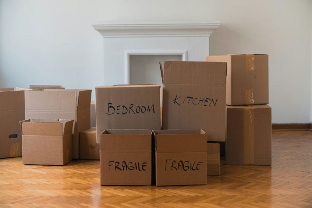 Pile of boxes stacking on empty room. In the background a white fireplace.